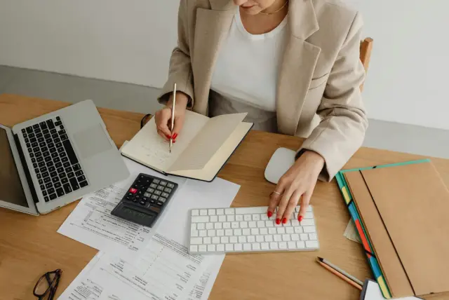 Mujer trabajando en una mesa con portátil, calculadora, cuaderno y documentos