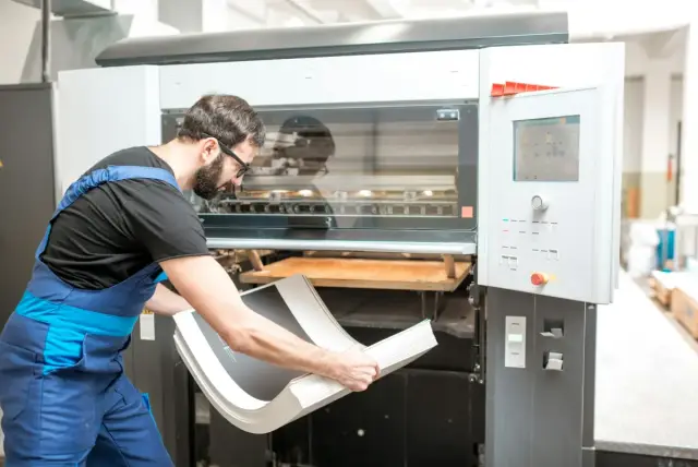 Operario colocando planchas en una máquina de impresión industrial
