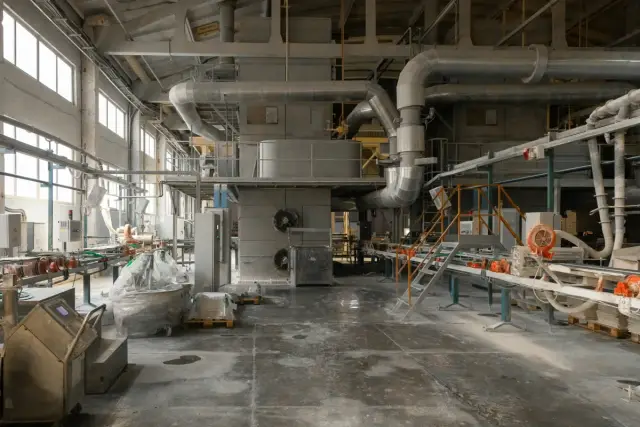 Nave industrial vacía con tuberías de ventilación y maquinaria al fondo