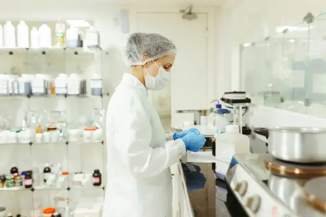 Técnica de laboratorio con bata, gorro y mascarilla manipulando productos