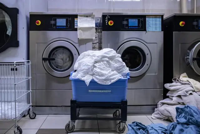 Lavadoras industriales con un cesto azul lleno de sábanas blancas