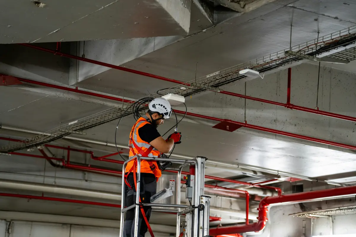 Técnico con casco y chaleco instalando cableado en el techo de un edificio